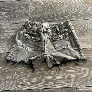 Grå jeansshorts från Gina Tricot - Snygga grå jeansshorts från Gina Tricot med råa kanter och slitna detaljer. Modellen har hög midja, praktiska fickor både fram och bak samt bälteshällor. Perfekt för dig som gillar en cool och avslappnad stil under sommaren.