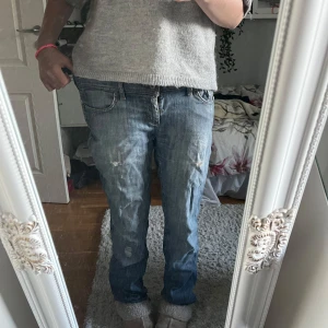 Blå slitna jeans - Säljer ett par blå jeans med coola slitningar och detaljer på benen. Modellen har klassisk femficksdesign, normal passform och boutcut ben. Jeansen är tillverkade i mjukt denimtyg som är skönt att bära hela dagen. säljer för de är för stora för mej