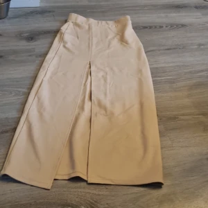 Beige långkjol från Bik Bok XS - Snygg beige långkjol från Bik Bok i storlek XS. Kjolen har en rak passform med slits framtill för extra rörelsefrihet. Tillverkad i mjukt tyg som känns skönt mot huden. Perfekt för dig som gillar stilrena och enkla plagg. Det är ett litet hål