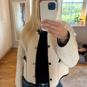 Vit quiltad jacka med svarta detaljer - Säljer en vit quiltad jacka med svarta knappar och svarta kantdetaljer. Jackan är superskön och har inga defekter💕