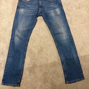 Blå Replay Rocco jeans comfort fit - Snygga blå jeans från Replay, modell Rocco med comfort fit. Klassisk femficksdesign, raka ben och ljusare tvättade partier framtill och baktill. Gula sömmar på bakfickorna ger en schysst detalj. Perfekta jeans för dig som gillar avslappnad stil.