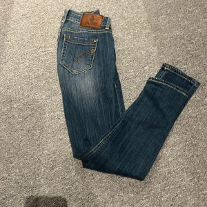 Dondup jeans - Snygga blå jeans från dondup med klassisk femficksdesign och cool läderpatch bak i midjan. Jeansen har kontrastsömmar och en rak passform som funkar till många olika stilar. Perfekt för dig som gillar en tidlös look med lite edge.