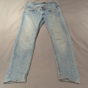 Lee Daren Zip Fly ljusblå jeans W28 L32 - Ljusblå jeans från Lee, modell Daren Zip Fly. Klassisk femficksdesign med dragkedja och raka ben. Jeansen har kontrastsömmar och en snygg tvättad look som ger en chill vibe. Passar dig som gillar tidlös stil och vill ha ett par jeans som funkar till allt.