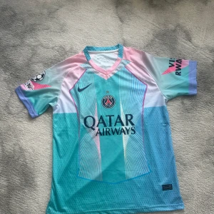 PSG x Nike kortärmad fotbollströja - Snygg PSG fotbollströja från Nike med Qatar Airways tryck. Tröjan har korta ärmar och coolt grafiskt mönster i turkos, rosa, lila och vitt. V-ringad krage med kontrastfärg och Champions League-märke på ärmen. Perfekt för dig som gillar unik design. Pris kan diskuteras vid snabb affär.