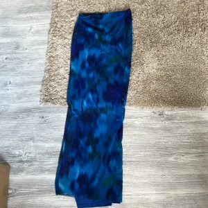 Blå mönstrad långkjol i polyester - Säljer en långkjol med coolt blått mönster i olika nyanser. Kjolen är gjord av mjuk polyester med lite stretch för skön passform. Perfekt för dig som gillar färgstarka plagg och vill sticka ut lite extra. Midjemodell och lätt material.