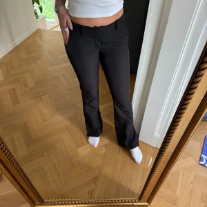 Svarta bootcut kostymbyxor låg midjade - Snygga svarta kostymbyxor med bootcut-snitt och låg midja. Byxorna har klassiska fickor fram och bak, bälteshällor och stängs med knapp och dragkedja. Perfekta för en clean och stilren look, passar till både sneakers och boots.