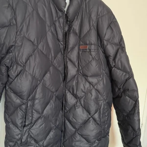  Peak Performance - Säljer en svart quiltad jacka från Peak Performance. Jackan har en dragkedja framtill och en diskret logotyp på bröstet. Perfekt för kyligare dagar med sin stilrena design och bekväma passform. Dragkedjan behövs lagas hos sömmerska men väldigt lätt och brukar vara hyfsat billigt att fixa 