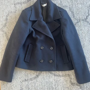 Marinblå skepparkavaj - Marinblå skepparkavaj med dubbelknäppning och bred krage. Jackan har långa ärmar och två framfickor. Perfekt vårjacka.  StlM men passar även XS-S .