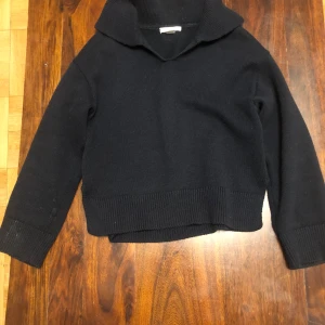 Svart stickad tröja från Gina Tricot - Säljer en svart stickad tröja från Gina Tricot. Tröjan har en hög krage och långa ärmar med ribbade muddar. Perfekt för kyligare dagar. Hör av dig vid intresse!