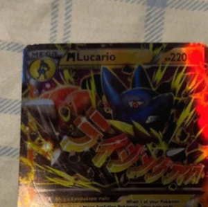 Mega Lucario Pokémonkort - Säljer ett Mega Lucario Pokémonkort med nummer 220. Kortet har en färgglad design med Lucario i fokus och japansk text. Baksidan har den klassiska Pokémon-designen med en Pokéball i mitten.