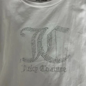 Vit t-shirt från Juicy Couture - Säljer en vit t-shirt från Juicy Couture med glittrande strassdetaljer. Perfekt för att lägga till lite glamour i vardagen! Är i storlek 14-15 år men jag skulle säga att den passar folk med XS/S även folk med M