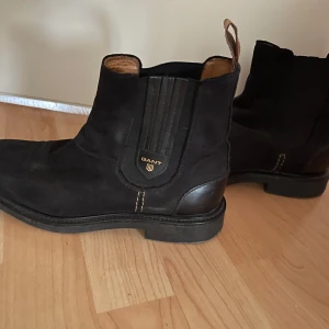 Svarta boots från Gant - Snygga svarta boots från Gant med elastiska paneler på sidorna för enkel på- och avtagning. Skorna har en robust sula och en diskret logga på sidan. Perfekta för en stilren look.