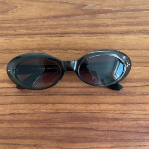 Svarta ovala solglasögon från Gucci - Snygga svarta ovala solglasögon från Gucci med mörka linser. De har en elegant design med märkets logotyp på skalmarna. Perfekta för en stilren look.