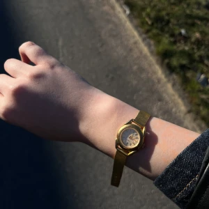Elegant guldfärgad klocka - Snygg guldfärgad klocka med en klassisk design. Klockan har en rund urtavla och ett matchande guldfärgat armband. Perfekt för att ge en touch av elegans till din stil.