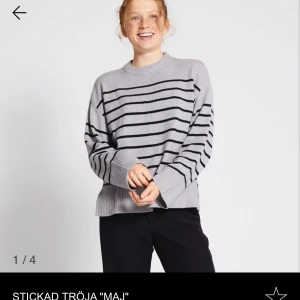 Grå randig stickad tröja 'Maj' - Säljer en stilren grå stickad tröja med svarta ränder. Tröjan har en avslappnad passform med långa ärmar och ribbade muddar. Perfekt för en mysig dag.