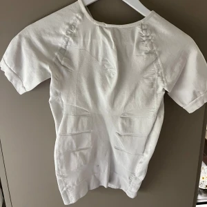 Vit kortärmad topp - Säljer en stilren vit topp med korta ärmar och unika sömdetaljer. Perfekt för en minimalistisk look. Toppen har en rund halsringning och är gjord i ett mjukt material.