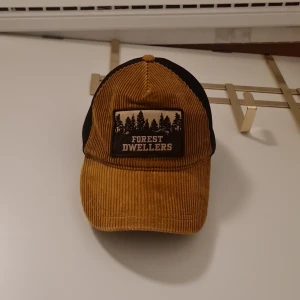 Brun manchesterkeps från Zara - Snygg brun manchesterkeps från Zara med svart baksida och ett coolt 'Forest Dwellers' märke framtill. Perfekt för en avslappnad stil med en touch av naturkänsla.