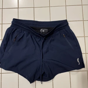 Marinblåa träningsshorts från RS Sports - Säljer ett par marinblåa träningsshorts från RS Sports. De har en elastisk midja med snörning och praktiska dragkedjefickor på sidorna. Perfekta för löpning eller gymmet!🏋️‍♀️🥰