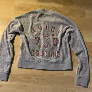 Grå zip-up från Juicy Couture - Säljer en grå zip-up från Juicy Couture med glittrande detaljer på ryggen. Jackan har långa ärmar och en dragkedja framtill. 