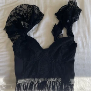Svart spetskorsett med volangdetaljer - Elegant svart korsett med vackra spetsdetaljer och volangprydda axelband. Perfekt för en stilfull look. Den har en figurnära passform och är tillverkad i ett mjukt material, skriv för fler bilder🤍🫶🏻