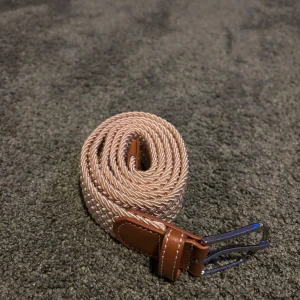 Beige flätat bälte med bruna detaljer - Snyggt beige flätat bälte med bruna skinnliknande detaljer och silverfärgat spänne. Perfekt för att ge en stilren touch till din outfit. Längden är 105cm