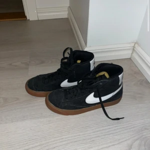 Svarta Nike sneakers med vit swoosh - Snygga svarta Nike sneakers med vit swoosh och brun sula. Skorna har snörning och en klassisk design som passar perfekt för vardagsbruk. Insidan har en röd Nike-logga. Använda två gånger så är i superbra skick, kostade 900 nya