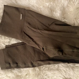  leggings från Aim'n - Snygga bruna/millitärgröna leggings från Aim'n med ribbad midja och detaljerade meshpaneler längs benen. Perfekta för träning eller en avslappnad dag. De har en tight passform som ger bra stöd och komfort.