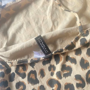 Leopardmönstrad kort klänning Gina Tricot - Snygg kort klänning från Gina Tricot med leopardmönster i beige, brunt och svart. Klänningen har smala axelband och figurnära passform, perfekt för dig som vill sticka ut. Materialet är mjukt och stretchigt för en bekväm känsla.