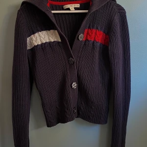 Mörkblå stickad kofta från Tommy Hilfiger - Säljer en snygg mörkblå stickad kofta från Tommy Hilfiger med knappar framtill. Den har vita och röda detaljer på bröstet och en ribbad struktur. Perfekt för kyliga dagar! 💙