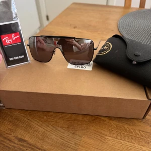 Ray-Ban svarta solglasögon - Snygga svarta solglasögon från Ray-Ban med hel lins och minimalistisk båge. Glasögonen har en modern, sportig look och är tillverkade i Italien. Perfekta för dig som vill sticka ut med en stilren accessoar. Ingen skador och fodral och puts duk följer med