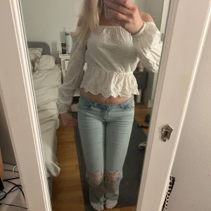 Vit blus med spetsdetaljer - Säljer en söt vit blus med spetsdetaljer och volangkant. Blusen har långa ärmar och en offshoulder-design som ger en romantisk känsla. Perfekt för vår och sommar!