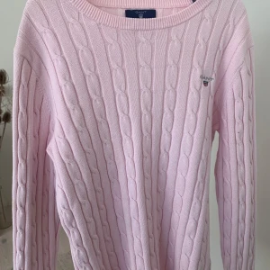 Rosa kabelstickad tröja från GANT - Säljer en söt rosa kabelstickad tröja från GANT. Tröjan har en klassisk rund hals och långa ärmar. Perfekt för en stilren och bekväm look. 💖