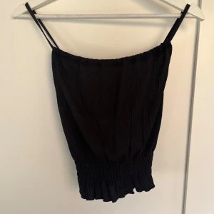 Svart linnetopp från Gina Tricot - Snygg svart linnetopp från Gina Tricot med smala axelband och elastisk nederkant. Banden bildar ett X i ryggen!