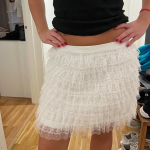 Vit spetskjol från Nerve - Säljer en superfin vit spetskjol från Nerve med flera lager volanger. Kjolen har en elastisk midja och är perfekt för en somrig look. Man kan även ha den som en topp om man skulle vilja det som man kan se på bilderna. Prislappen är kvar och är aldrig använd! 