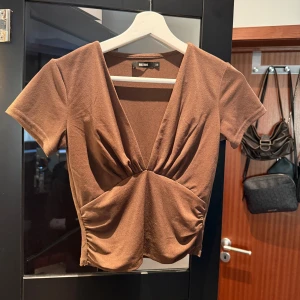 Brun v-ringad topp  - Säljer en snygg brun topp från BikBok med v-ringning. Toppen har korta ärmar och en figurnära passform. Perfekt för en stilren look! [Storlek XS] 🤎