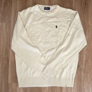 Vit tröja från Polo Ralph Lauren - Säljer en stilren vit tröja från Polo Ralph Lauren med deras ikoniska logga broderad på bröstet. Tröjan har långa ärmar och ribbade muddar vid ärmslut och nederkant. Perfekt för en klassisk och avslappnad look.