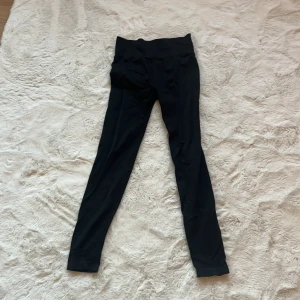 Svarta leggings från New Apparel - Säljer ett par svarta leggings från New Apparel i storlek M. De är tillverkade av 92% polyamid och 8% spandex, vilket ger en stretchig och bekväm passform. Perfekta för både träning och vardag.