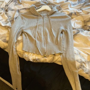 Beige croppad hoodie från Foster Knitwear - Säljer en beige croppad hoodie från Foster Knitwear. Den har en dragkedja framtill och långa ärmar. Perfekt för en avslappnad stil. Hör av dig vid intresse!