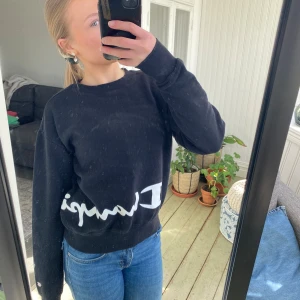 Svart sweatshirt från Champion - Säljer en svart sweatshirt från Champion med vit logga framtill. Tröjan har långa ärmar och en rund halsringning. Perfekt för en avslappnad stil. Hör av dig vid intresse!