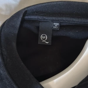 Svart tröja med grafiskt tryck - Snygg svart tröja från MCQ med ett unikt grafiskt tryck i flera färger. Tröjan har långa ärmar och en rund halsringning. Perfekt för dig som vill sticka ut med en cool design.