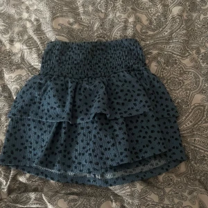 Blå kjol med volanger från Zara - Söt blå kjol från Zara med små mörkblåa blommor och volanger. Kjolen har en elastisk midja för bekväm passform och är perfekt för en avslappnad stil. Den är kort och har inbyggda shorts