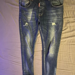 Dsquared 2 jeans - Säljer ett par blå jeans med slitningar på framsidan. De har en klassisk femficksdesign och en knappgylf. Perfekta för en avslappnad stil.