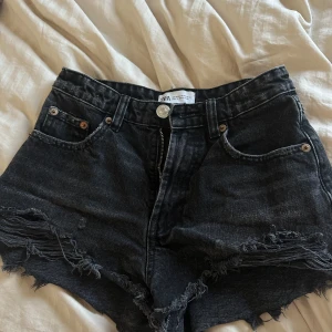 Svarta jeansshorts från Zara - Säljer ett par svarta jeansshorts från Zara med fransiga kanter och hög midja. Perfekta för en avslappnad stil. De har klassiska fem fickor och en dragkedja framtill.