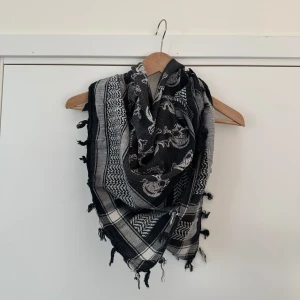 Svart och vit sjal med dödskallemönster - Snygg svart och vit sjal / scarf / halsduk med ett coolt dödskallemönster. Den har fransar längs kanterna och ett rutigt mönster som ger en extra touch. Perfekt för att ge din outfit en edgy stil.
