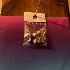 Färgglada örhängen med pärlor - Säljer ett par unika örhängen med färgglada pärlor i blått, rosa och vitt. Perfekta för att ge en färgklick till din outfit. Kommer i en praktisk förpackning.