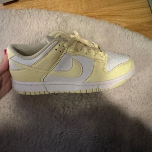 Nike Dunk i gult och vitt - Säljer ett par Nike Dunk sneakers i en fräsch kombination av gult och vitt. Skorna har en klassisk design med snörning och rund tå. Perfekta för en stilren och sportig look.