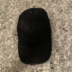 Svart keps med GG-mönster - Snygg svart keps med det ikoniska GG-mönstret. Perfekt för att ge din outfit en lyxig touch. Kepsen har en klassisk design med justerbar passform.