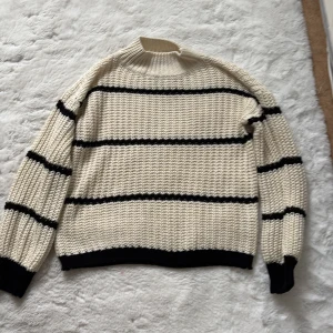 Vit och svart randig stickad tröja - Säljer en snygg vit stickad tröja med svarta ränder. Tröjan har en ribbad krage och långa ärmar med ribbade muddar. Perfekt för kyliga dagar! köpt för 400kr säljs för 150kr