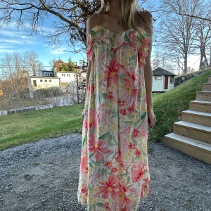 Blommig sommarklänning - Säljer en färgglad blommig sommarklänning med volangdetaljer. Klänningen har en avslappnad passform, smala axelband och ett vackert blommönster i rosa, grönt och gult. Prislappen finns kvar och är helt oanvänd☺️