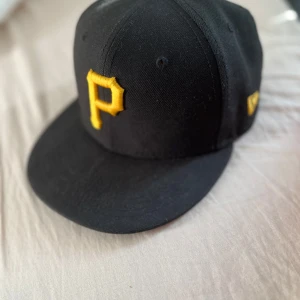 Svart keps från New Era - Snygg svart keps från New Era, modell 59FIFTY. Kepsen har en broderad logotyp baktill och är tillverkad i 100% polyester. Perfekt för en stilren look.